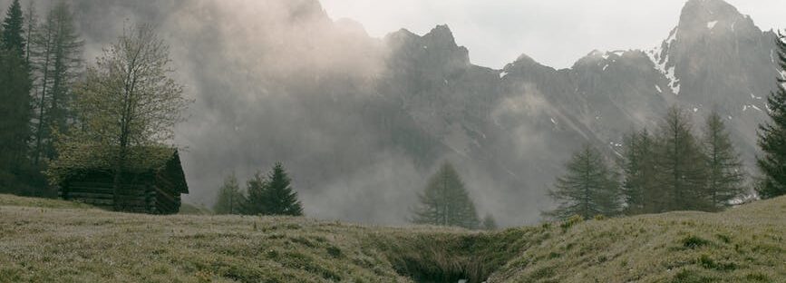 lonesome house on foggy valley against massive mountain ridge