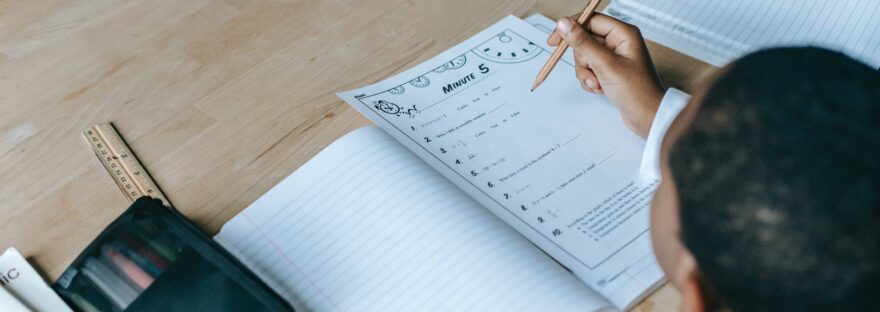 crop faceless black schoolboy writing in copybook in classroom