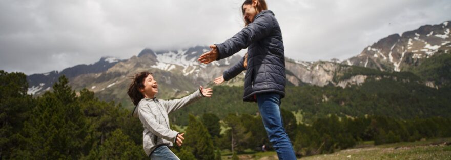 woman and child playing on green grass field near mountain