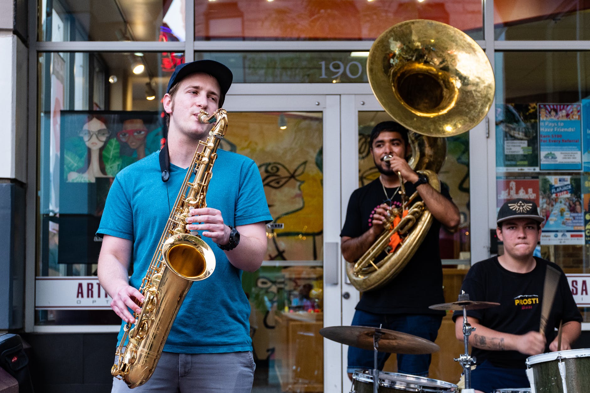 three man playing drums and wind instruments in front of store