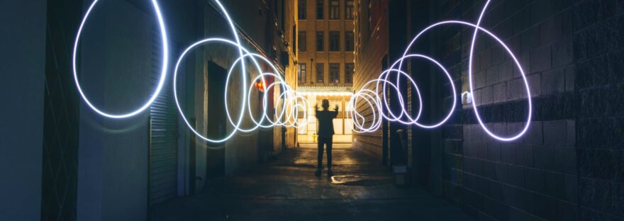 silhouette of person making circles with flashlight on dark street
