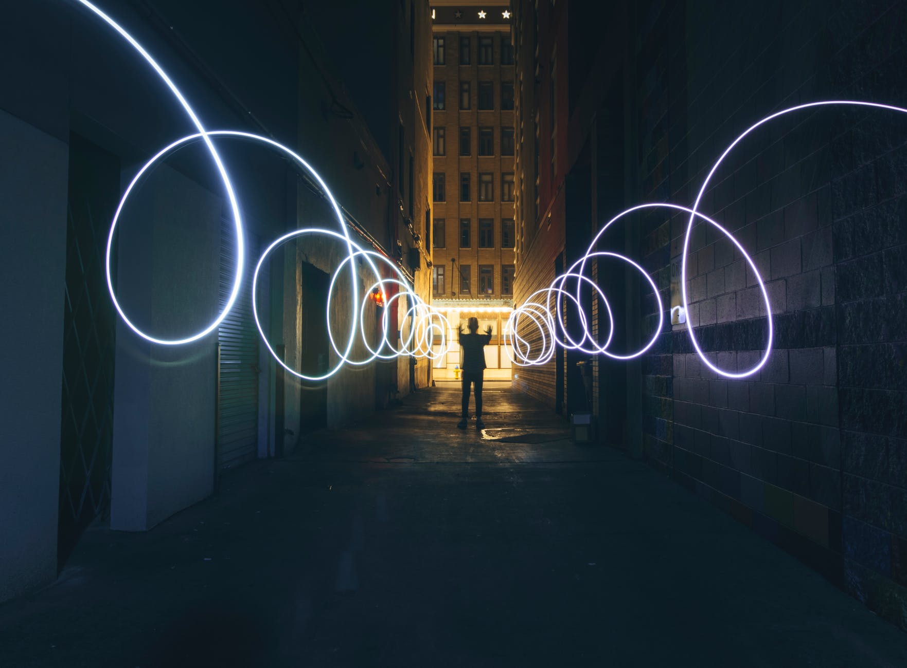 silhouette of person making circles with flashlight on dark street