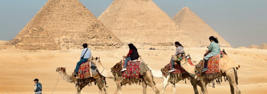 four people riding on camels across the pyramids