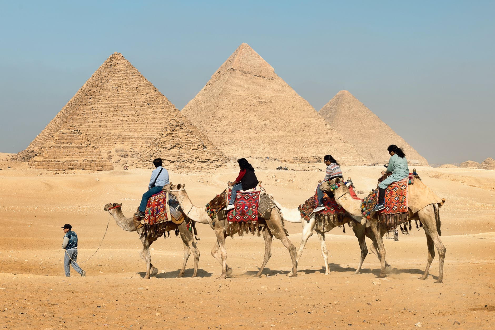 four people riding on camels across the pyramids