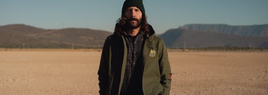 bearded man standing in desert valley surrounded by hills