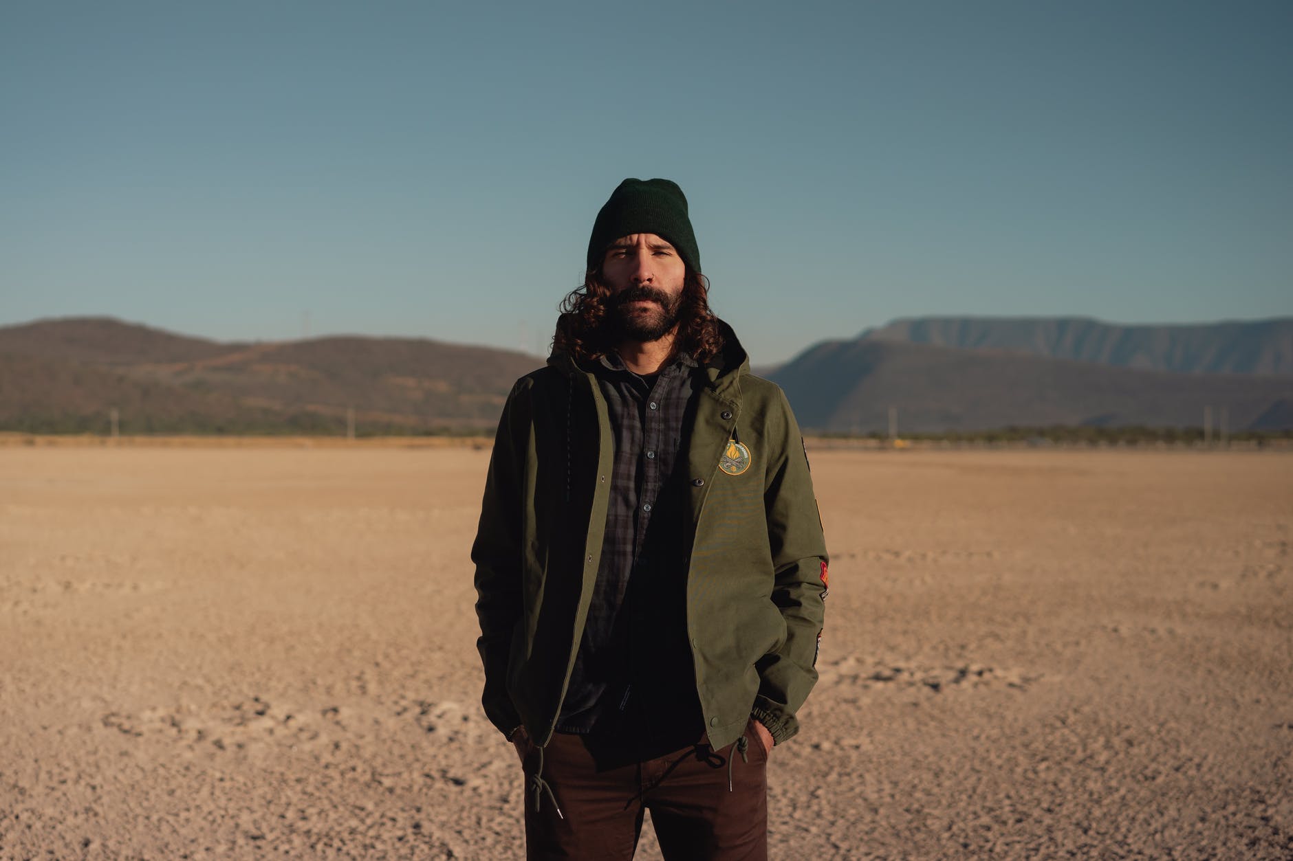 bearded man standing in desert valley surrounded by hills