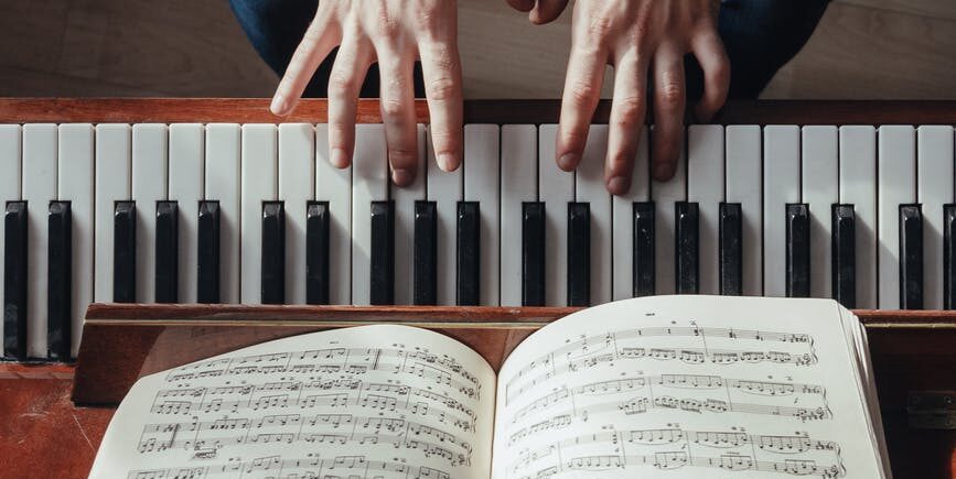 crop pianist playing piano with sheet music on stand