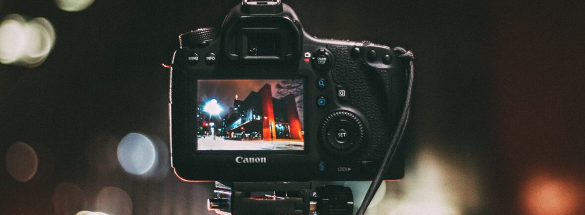 selective focus photography of black canon camera displaying photo of red and black building