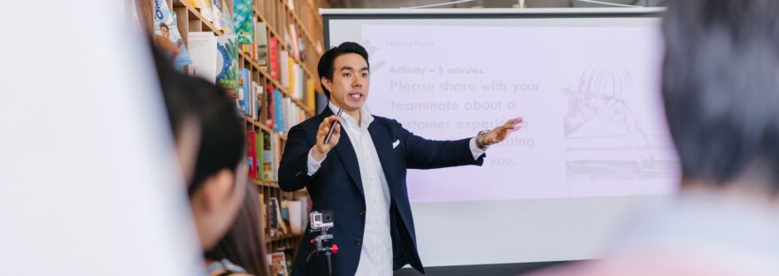 man in suit jacket standing beside projector screen