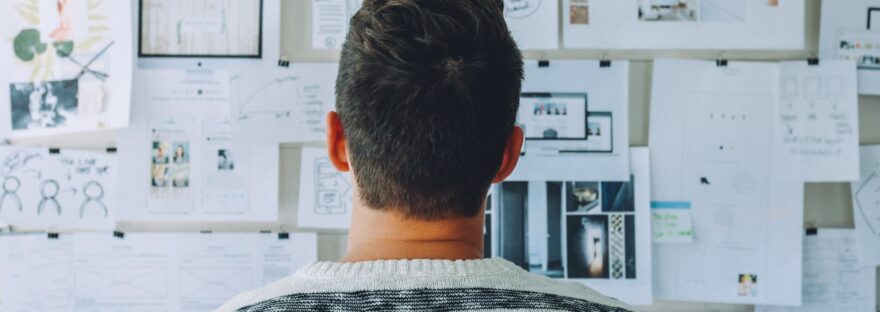 man wearing black and white stripe shirt looking at white printer papers on the wall