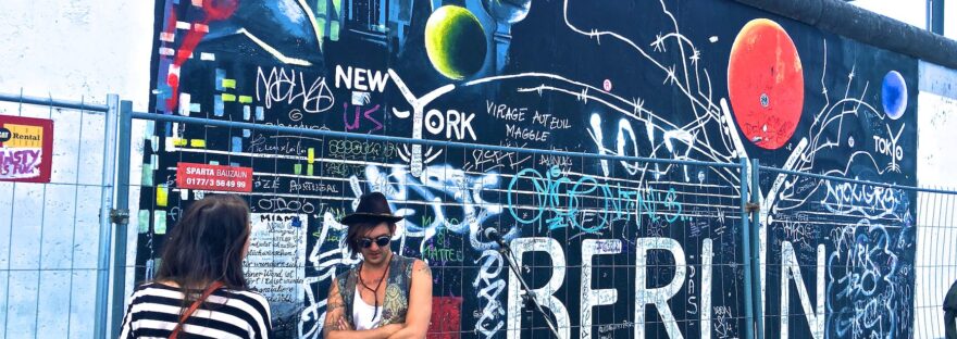 man wearing black waistcoat and white tank tops standing near a mural